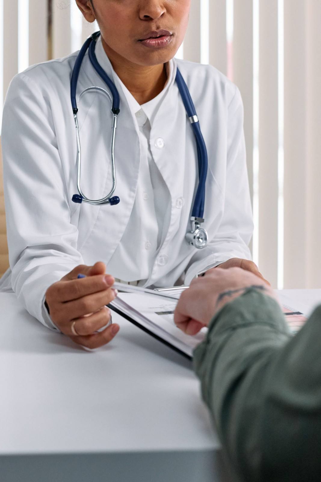 Un médico con bata blanca atiende a un paciente en una mesa con documentos médicos.